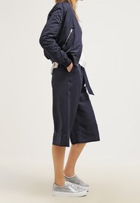 Námořnická bomber bunda se stříbrným zipem, spárovaná s širokými námořnickými kalhotami a metalickými stříbrnými teniskami. Hladká tkanina, volný střih.