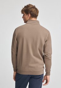 Pullover marrone con colletto alto, maniche lunghe e tessuto testurizzato. Finitura liscia, colore solido e polsini e orlo a coste.