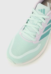 Svijetloplata sportska tenisica s mrežastim gornjim dijelom, vezicama zavezanima i tirkiznim logotipom na jeziku i boku, fotografirana na bijeloj pozadini.