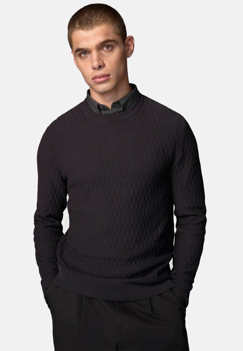 Mørk tekstureret sweater med ribbet mønster, rund halsudskæring og lange ærmer, parret med en skjorte med krave nedenunder.