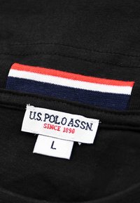 Black fabric with U.S. Polo Assn. size L label and red, white, and blue striped design near the neckline.