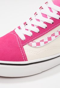 Vaaleanpunaiset mokkanahka- ja kerma-kanvas-tennarit valkoisilla nauhoilla, joissa on ruudullinen korostuslogo ja musta pohjareuna.