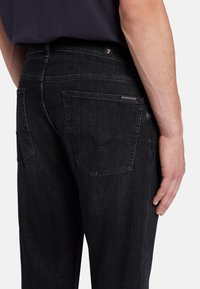 Jeans in denim nero con taglio dritto, dotati di tasche posteriori, leggere abrasioni e un'etichetta con il marchio sulla vita.