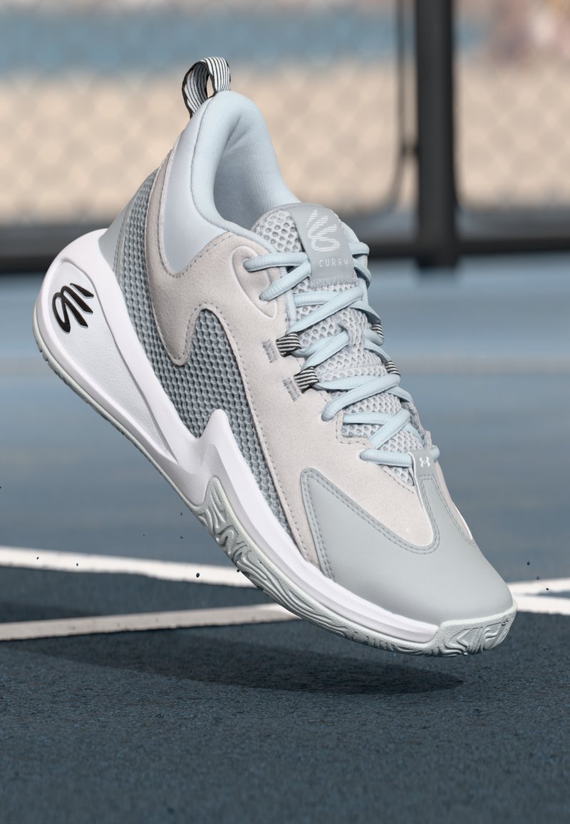 Chaussures de sport gris clair avec une tige en mesh, des accents en daim et une semelle en caoutchouc. Présente un logo sur le talon et un design de lacets distinctif.