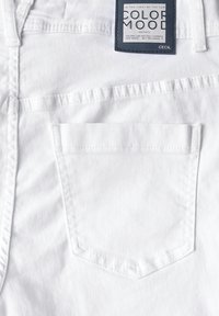 Le tissu en denim blanc présente une poche arrière de forme triangulaire avec une étiquette de marque indiquant "COLOR MOOD" et "CECIL."