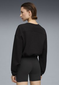 Sort cropped sweatshirt med lange ærmer, afslappet pasform og ribbet kant, parret med sorte tætsiddende shorts. Glat tekstur.