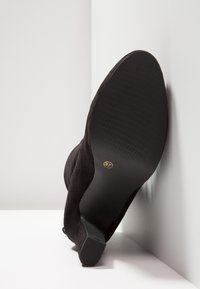 Bottine en daim noir avec bout pointu, talon étroit, semelle texturée, et étiquette de taille « 37 » visible à l'intérieur de la semelle.