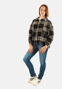 Chaqueta de cuadros negra y gris con dobladillo desflecado, combinada con vaqueros azules y zapatillas blancas con acentos azules.