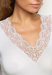 Top bianco con scollatura a V profonda, arricchita da un intricato bordo in pizzo con motivo floreale, che esalta il decolletè con una delicata texture.