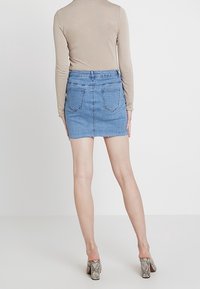 Mini-jupe en denim bleu clair avec un ourlet brut, dotée d'une coupe ajustée et de poches arrière. Associée à un haut beige à manches longues et des talons imprimés serpent.