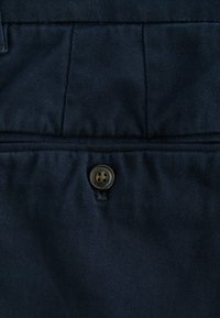 Materialul navy are un model texturat și un buton maro vizibil în partea de jos. Două cusături orizontale deasupra butonului.