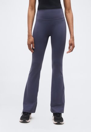 Person wearing high-waisted, dark gray flared pants and black sneakers standing against a plain light background.