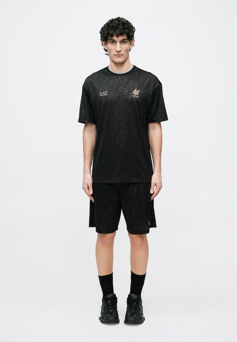 Melnas sporta apģērbs ar īsām piedurknēm un šortiem. Abi gabali rotāti ar sešstūra rakstu un smalku zelta logo. Izskatu papildina melni apavi.