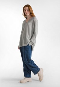 Grauer V-Ausschnitt-Pullover aus strukturiertem Stoff, kombiniert mit lockeren blauen Jeanshosen. Das Outfit wird durch beigen klobigen Sneakers abgerundet.