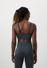 Tumši pelēkās sporta krūšturis ar regulējamām siksnām, platu joslu un teksturētu audumu. Pāris ar atbilstošām augstām legingām no tā paša materiāla.