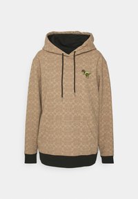 Sweat à capuche beige avec poignets et ourlet vert foncé, motif subtil, cordons noirs et petit dinosaure vert brodé sur la poitrine.