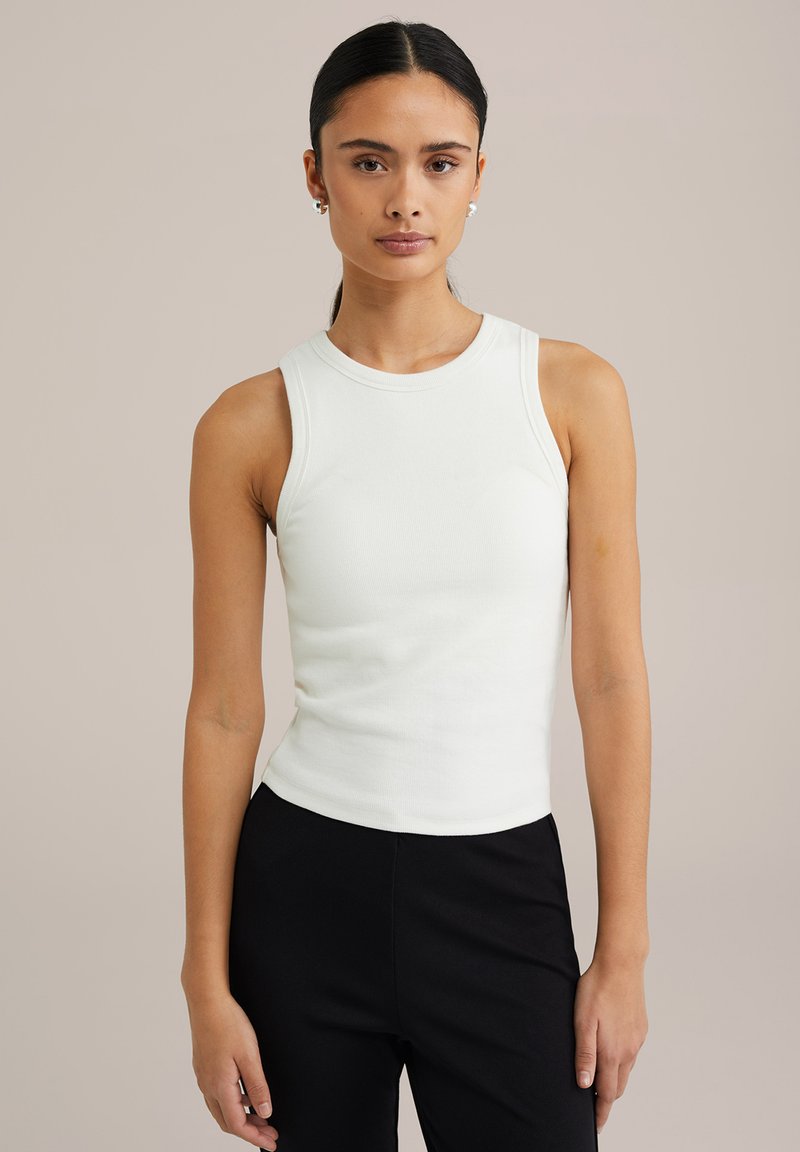 Hvid ribbet tanktop med rund halsudskæring og ærmeløst design, tætsiddende form, parret med sorte bukser for kontrast.