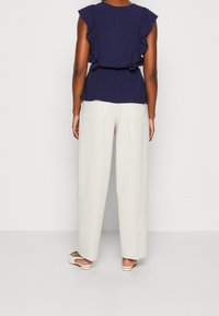 Námořnická halenka s volánky, která má přiléhavý pas a volný střih, spárovaná s krémovými kalhotami širokého střihu. Boty jsou bílé s jemnými detaily na pásku.