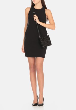 Abito nero senza maniche dal design aderente, abbinato a una borsa nera testurizzata con paillettes. Il modello indossa scarpe con tacchi alti nere.