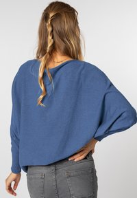 Blauer, locker sitzender Pullover mit weitem Ausschnitt und langen Ärmeln, aus strukturiertem Strickstoff, kombiniert mit grauen, enganliegenden Jeans.