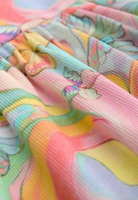 Tissu doux côtelé avec des motifs floraux pastel et abstraits dans des tons de rose, jaune, vert, bleu et orange, montrant de légers plis et une texture délicate.