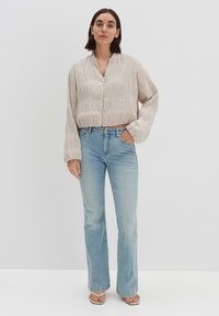 Light beige cropped jacket with textured stripes and zipper, paired with light blue flared jeans and flat sandals. Simple design and casual fit.