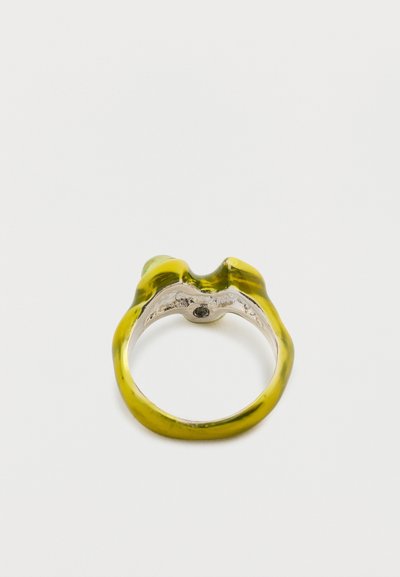 Dzeltena un zaļa sveķu gredzens ar viļņotu dizainu, kuram ir gluda virsma un metāliska sudrabota iekšpuse. Detalizācija ietver mazu melnu akmeni.