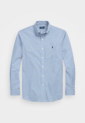 Camisa abotoada com padrão xadrez azul e branco, mangas longas e colarinho clássico. Apresenta um pequeno logotipo no peito.