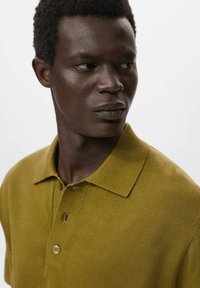 Olivgrön polo t-shirt i stickat material, med en ribbad krage, tre-knappars placket och ett texturerat mönster framtill.