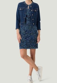 Jeansjacke mit cropped Design, goldenen Knöpfen, zwei Brusttaschen; marineblaues Kleid mit gesprenkelt floralem Muster in Blau, Grün und Weiß; silberne Sneaker.
