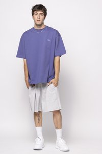 Oversized purple t-shirt with a logo, paired with gray knee-length shorts. White sneakers and ankle-length socks complete the outfit.