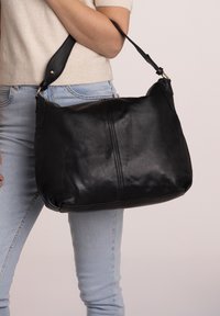 Borsa a tracolla in pelle nera con texture liscia, forma curva e tracolla regolabile, caratterizzata da una cucitura centrale.