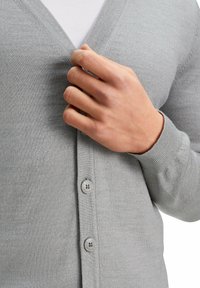 Cardigan grigio chiaro realizzato in morbido tessuto, con design a scollo a V, chiusure con bottoni e polsini a costine. Texture liscia con cuciture sottili.