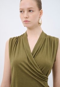 Olivově zelený top bez rukávů s draped wrap designem, s měkkou texturou látky a nařasenými detaily na ramenech.