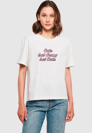 T-shirt in cotone bianco con maniche corte, caratterizzato da un design grafico in rosa che recita "Carina ma Sgargiante ma Carina." Vestibilità rilassata.