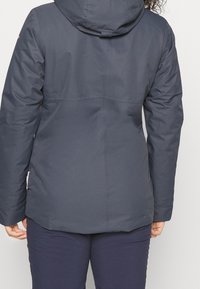 Granatowa kurtka ocieplana z kapturem, o gładkiej fakturze i minimalnym przeszyciu. Projekt zawiera prosty krój i skośne szwy.