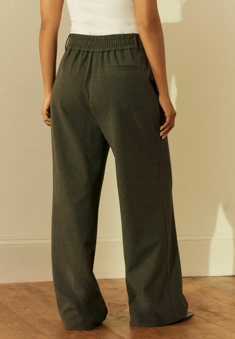 Koolgrijze wijde broek met een elastische tailleband, voorzien van een enkele achterzak en een geweven textuur, tentoongesteld op een houten vloer.