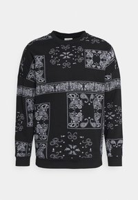 Sudadera negra con patrones de paisley blancos, con cuello redondo, mangas largas y un tejido suave y texturizado.