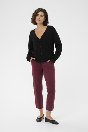 Cardigan noir en tricot avec un col en V et fermeture à boutons, associé à un pantalon court bordeaux et des ballerines noires. Design minimaliste.