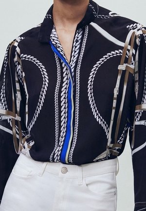 Black shirt with white chain design and blue accents, featuring a collared neckline and beige harness details overlaid.