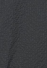 Surface noire texturée avec un motif de grille subtil et une pliure diagonale irrégulière traversant le tissu.