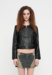 Μαύρο cropped δερμάτινο μπουφάν με ασημένιες καρφίτσες κατά μήκος του μπροστινού μέρους και των μανικιών, συνδυασμένο με μίνι φούστα τζιν με πολλούς τόνους.