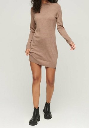 Brązowa sukienka z dzianiny z długim rękawem, wysokim dekoltem, dopasowanym krojem i lekko asymetrycznym dołem, w zestawieniu z czarnymi botkami za kostkę.