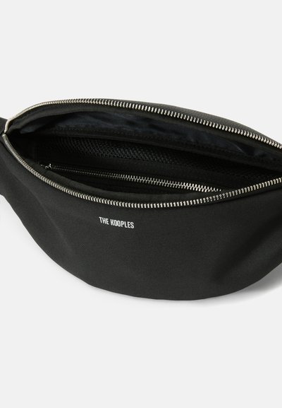 Black canvas fanny pack with silver zipper, featuring a logo in white. Interior includes a mesh pocket for organized storage.