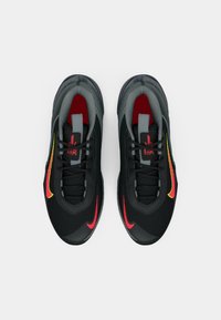Pár čiernych atletických topánok s červenými a žltými logami Swoosh, čiernymi šnúrkami a šedým vnútorným podšívkou, zhora na bielom pozadí.