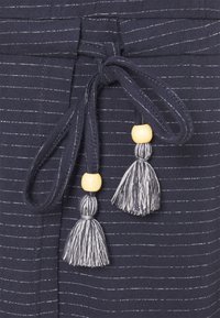 Mörkblått tyg med tunna vita ränder; har en knytet midja med tv å tofsar, varje prydd med en träperla.