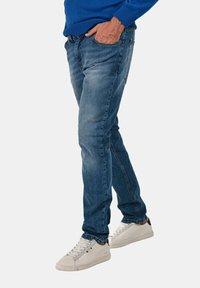 Jeans in denim a gamba dritta di colore azzurro chiaro con lieve scoloritura. Presentano tasche frontali e accenti di cucitura rossa. Indossati con sneaker bianche.