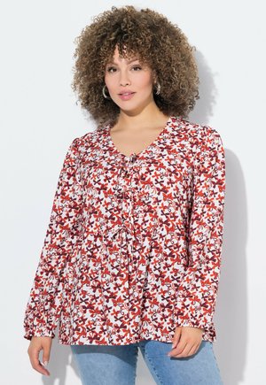 Blouse à manches longues avec un motif floral rouge et violet sur fond blanc, dotée d'un col ras du cou et de détails à cordon à l'avant.