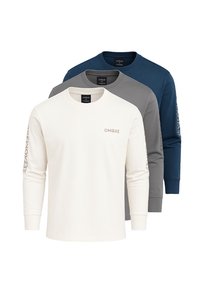 Tři trička s dlouhým rukávem a kulatým výstřihem v bílé, šedé a námořnické modři se šedým textem "OMBRE" na hrudi a rukávu, naskládána jedno na druhé.