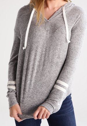 Sudadera gris de mangas largas con cuello en V y cordones blancos. Presenta acentos de rayas blancas en las mangas. Tejido suave y texturizado.